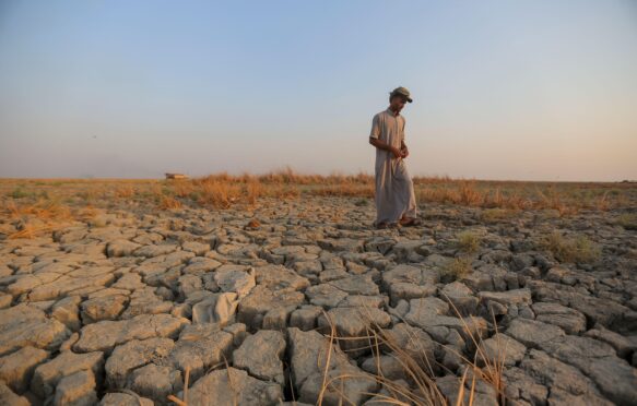 A fisherman walks across a dry patch of land after drought in the marshes of southern Iraq, Dhi Qar province. Image ID: 2M9TRTP.